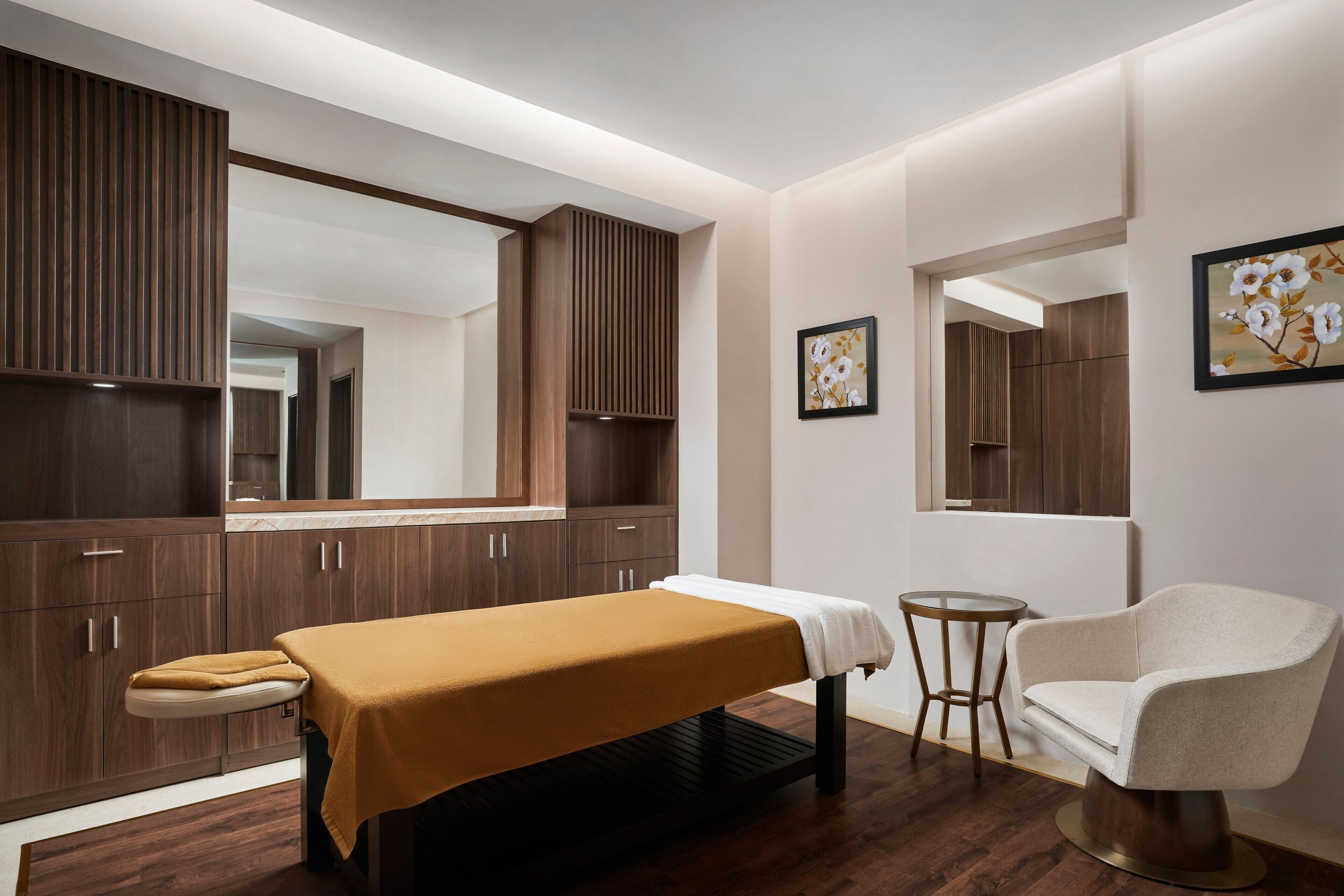 A modern room with a massage table, a white armchair, and wooden cabinets.