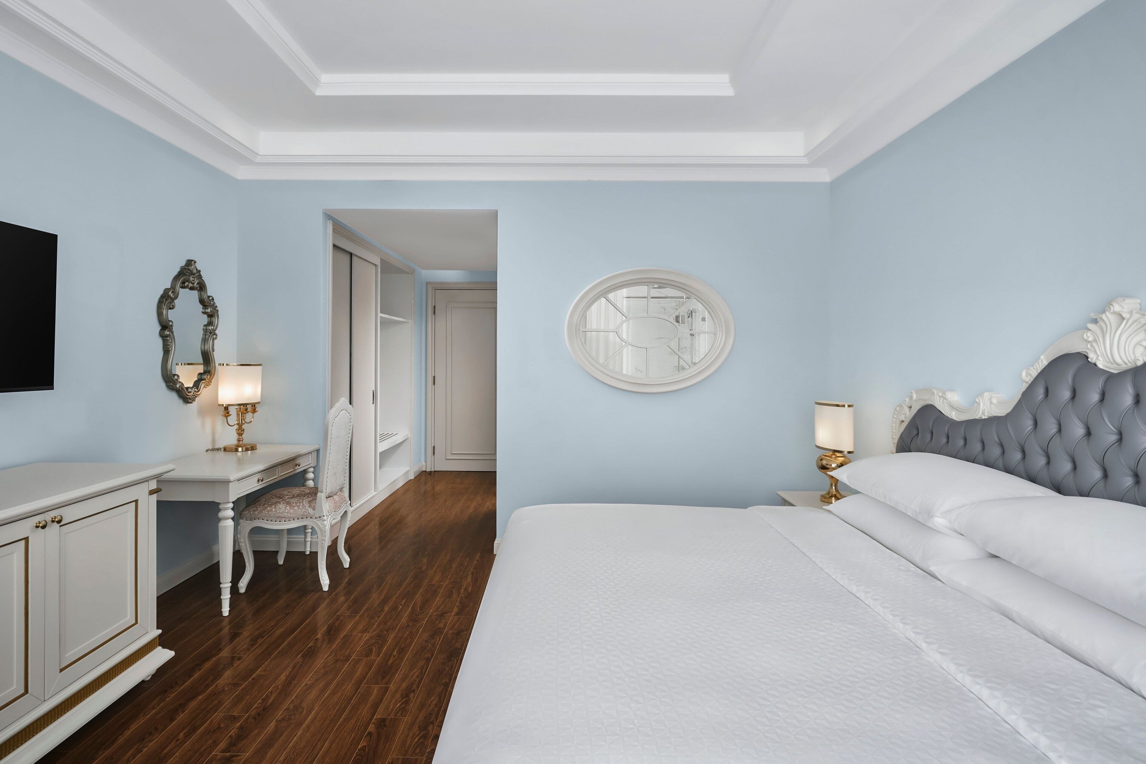A bedroom with a large bed, a desk with a chair, a mirror, and a round wall decoration.