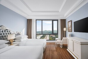 Habitación de hotel con dos camas, un ventanal con vistas a un río y colinas, un televisor de pantalla plana y un aparador blanco.
