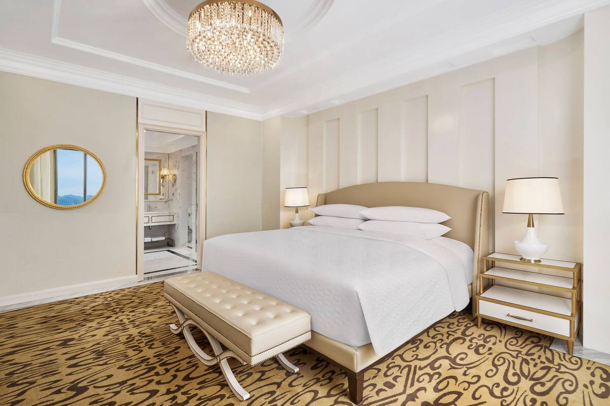 Une chambre spacieuse avec un grand lit, un banc, une table de chevet et un lustre.