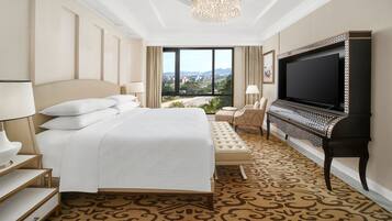 A hotel room with a large bed, a television, a seating area, and a view of the city.