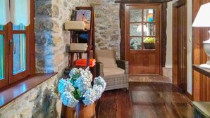 A stone-walled room with wooden floors, a wicker chair, a wooden bookshelf, and a door with a window.