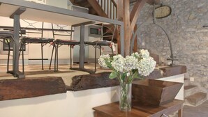 A rustic interior with a wooden staircase, a stone wall, and a dining area with metal chairs and a wooden table.