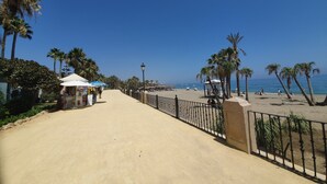 A beach promenade with palm trees, a kiosk, and a beach in the background.