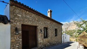 A stone building with a large wooden door, two windows, and a chimney.