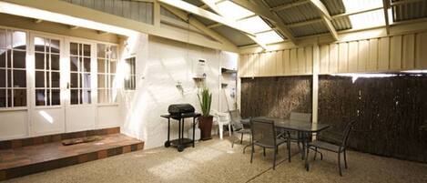A covered patio area with a table and chairs, a potted plant, and a grill.