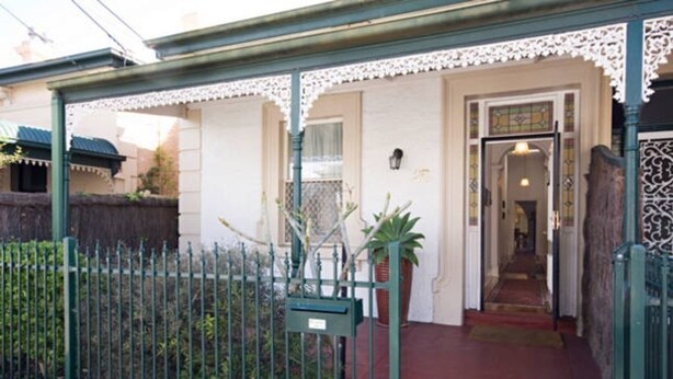 Una casa tradicional con fachada blanca, cercado de metal verde y entrada roja.
