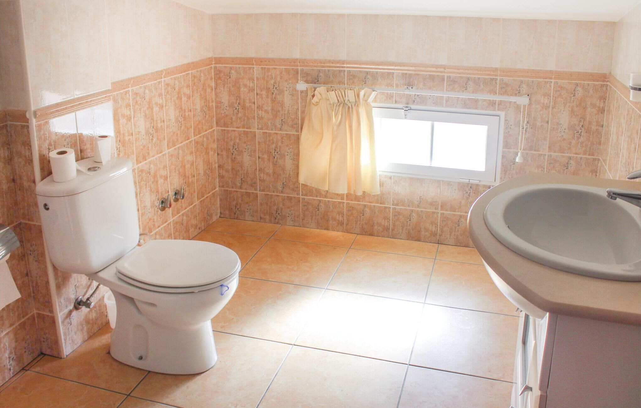 Un baño con inodoro, ventana con cortina y lavamanos.