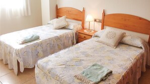 Une chambre double avec deux lits simples, chacun agrémenté de draps à motifs floraux et d’une tête de lit en bois. Une table de chevet avec une lampe se trouve entre les deux lits.