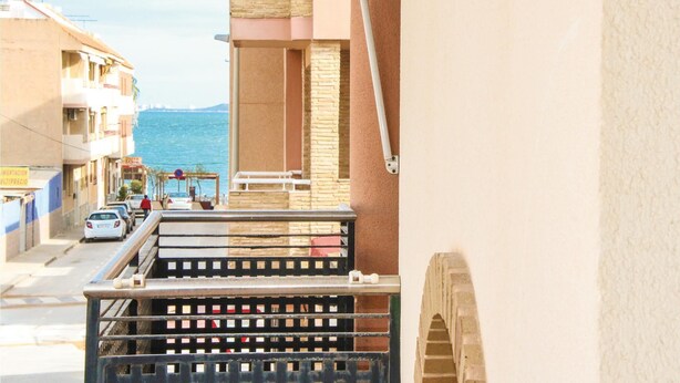 Un balcon donnant sur la mer, une rue bordée de voitures garées et des immeubles dotés de balcons.