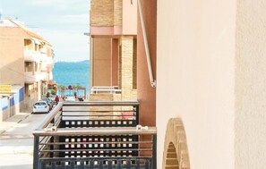 Un balcon donnant sur la mer, une rue bordée de voitures garées et des immeubles dotés de balcons.