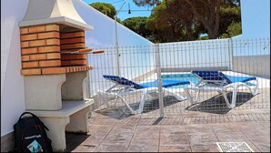 Un área de barbacoa con horno de ladrillo, una piscina con sillas de descanso y un árbol al fondo.