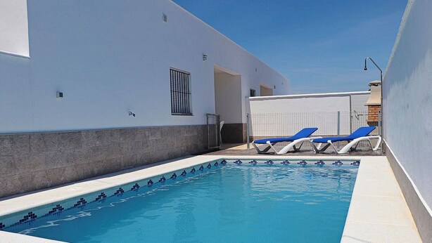 Una piscina con dos tumbonas y un área techada.