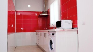 Una cocina pequeña con baldosas rojas y blancas, microondas, lavadora y lavamanos.