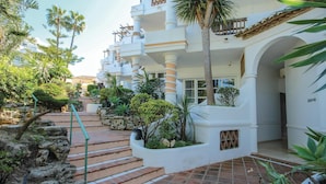 Un hotel de varios pisos con una escalera central, rodeado de abundante follaje y palmeras.