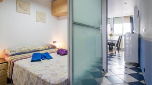 Un dormitorio con dos camas, una mesita de noche con una lámpara y vistas a la cocina y el comedor a través de una puerta de vidrio.