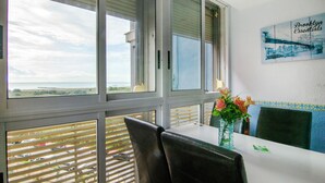 Una habitación con vista al océano, una mesa con sillas, un florero con flores y un cuadro en la pared.