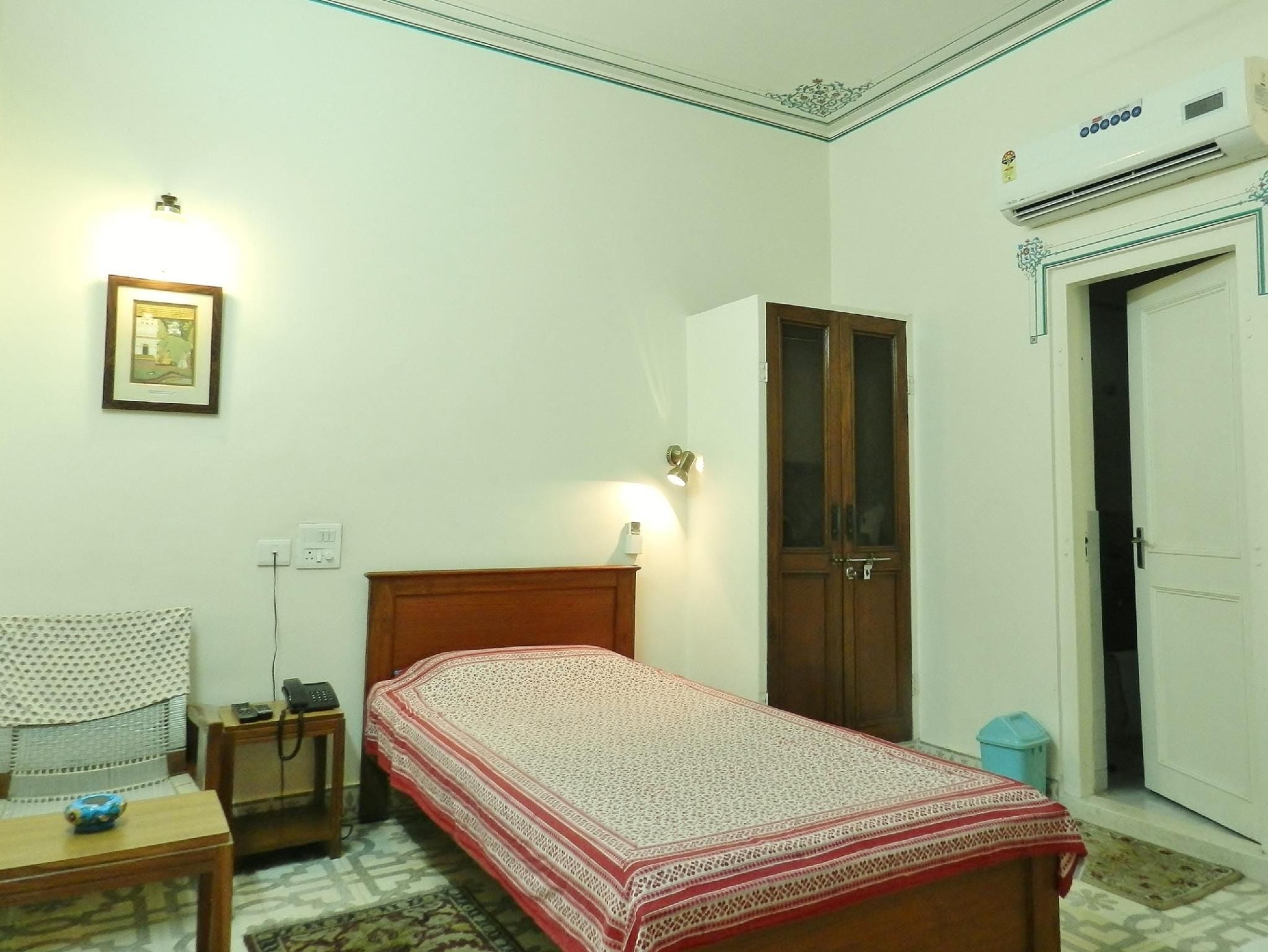 Un dormitorio con una cama individual, un armario, una mesita de noche con lámpara, una silla y un cuadro enmarcado en la pared.