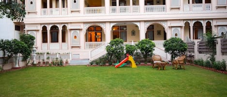 Un edificio de varios pisos con un patio central, ventanas arqueadas y una zona de juegos infantiles.