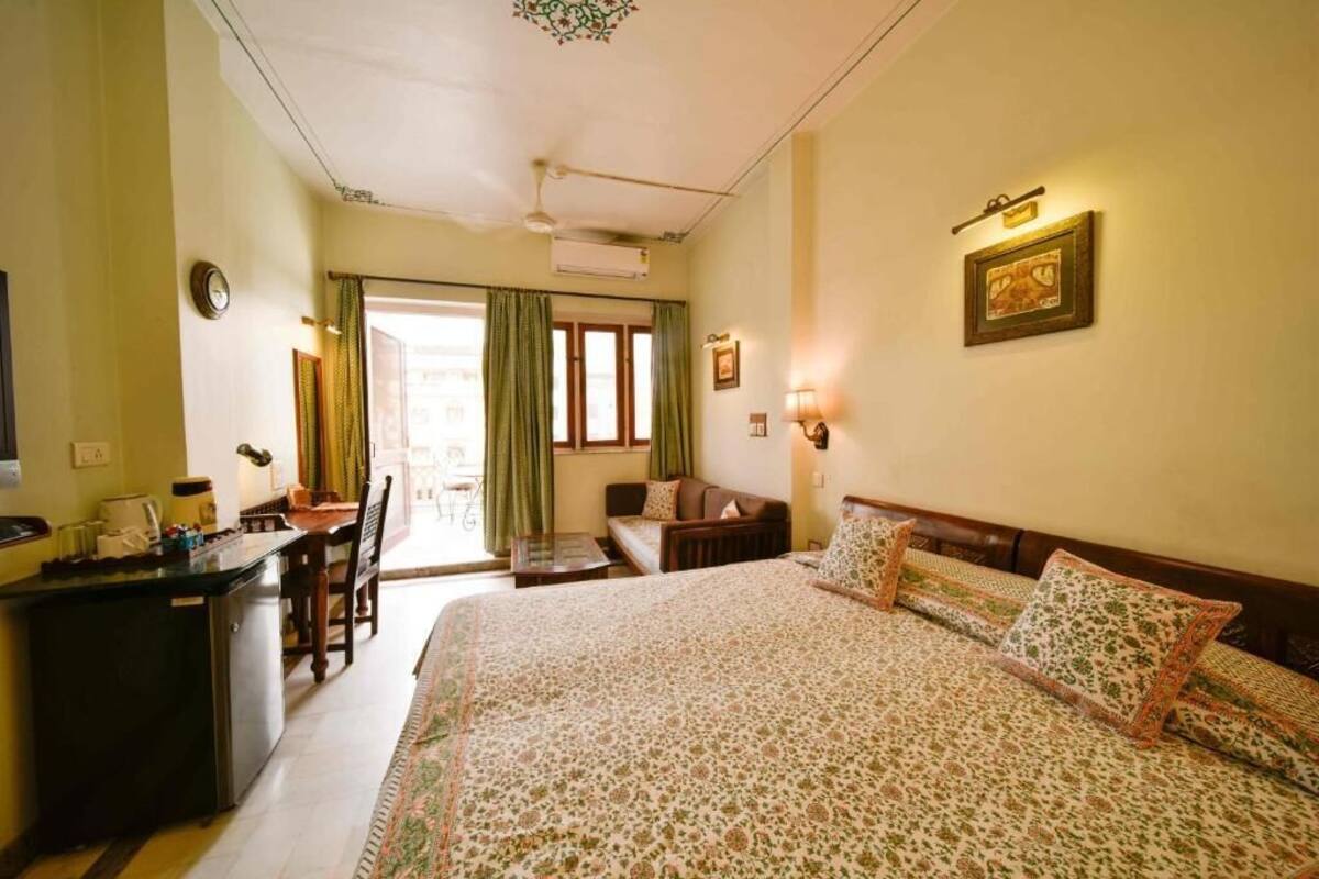Ein Hotelzimmer mit Bett, Schreibtisch, Stuhl, Nachttisch, Wanduhr und einem Fenster mit Vorhängen.