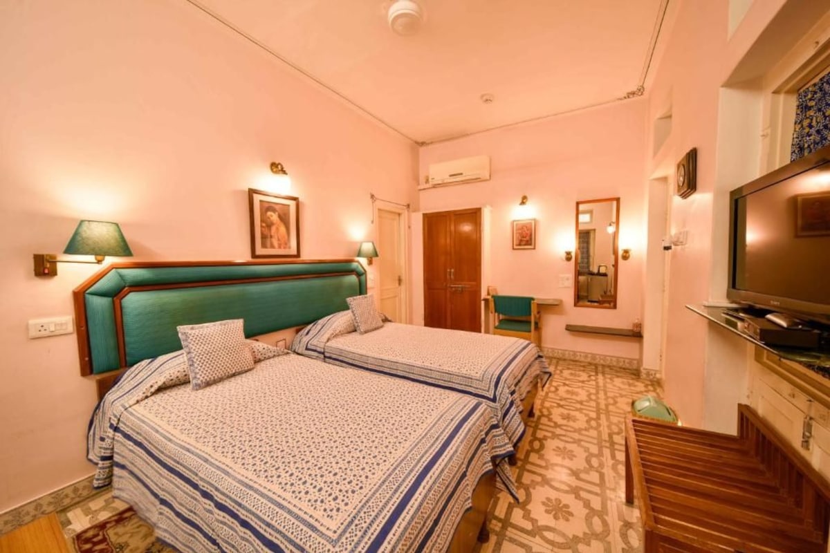 Habitación de hotel con dos camas, televisión, escritorio y espejo.