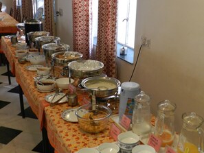 A buffet table with various food items and labeled containers, a window with curtains, and a tiled floor. - Hotel Arya Niwas, Jaipur (Jaipur)
