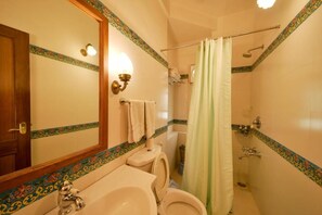 A bathroom with a toilet, sink, shower, and a mirror with a decorative border.