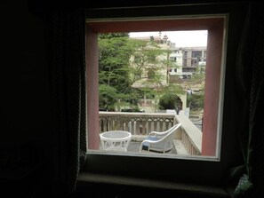 Ein Balkon mit zwei weißen Korbstühlen und einem kleinen Tisch, mit Blick auf eine Wohngegend mit Bäumen und Gebäuden.