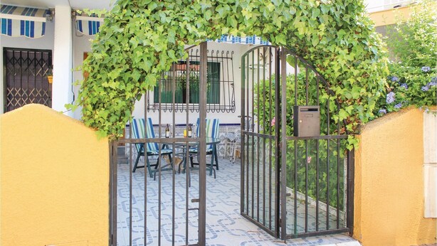 Un patio amurallado con suelo de baldosas, una mesa con sillas y una zona de estar cubierta.