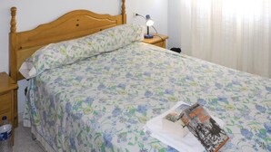 Un dormitorio con cama de madera, colcha estampada y una lámpara de noche, además de un libro sobre la cama.