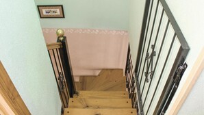 Una escalera de madera con barandilla metálica, un muro rosa y un cuadro enmarcado sobre la barandilla.