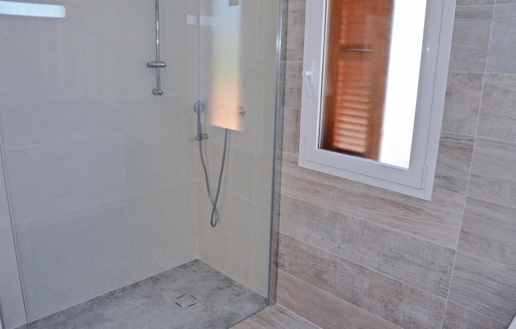 A glass-enclosed shower area with a tiled floor and a window with blinds.