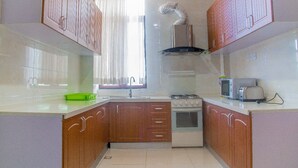 A kitchen with wooden cabinets, a gas stove, a microwave, and a toaster. - PCG Gisimenti Apartment (Kigali)