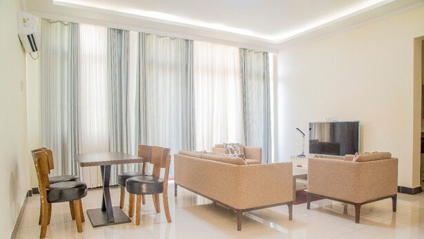 A modern living room with a sofa, two armchairs, a dining table with chairs, and a flat-screen TV. - PCG Gisimenti Apartment (Kigali)