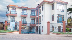 A multi-story building with a gated entrance, balconies, and a sign indicating it is an apartment complex. - PCG Gisimenti Apartment (Kigali)