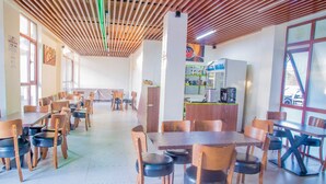 A spacious dining area with wooden tables and chairs, a counter with a coffee machine, and large windows providing natural light. - PCG Gisimenti Apartment (Kigali)