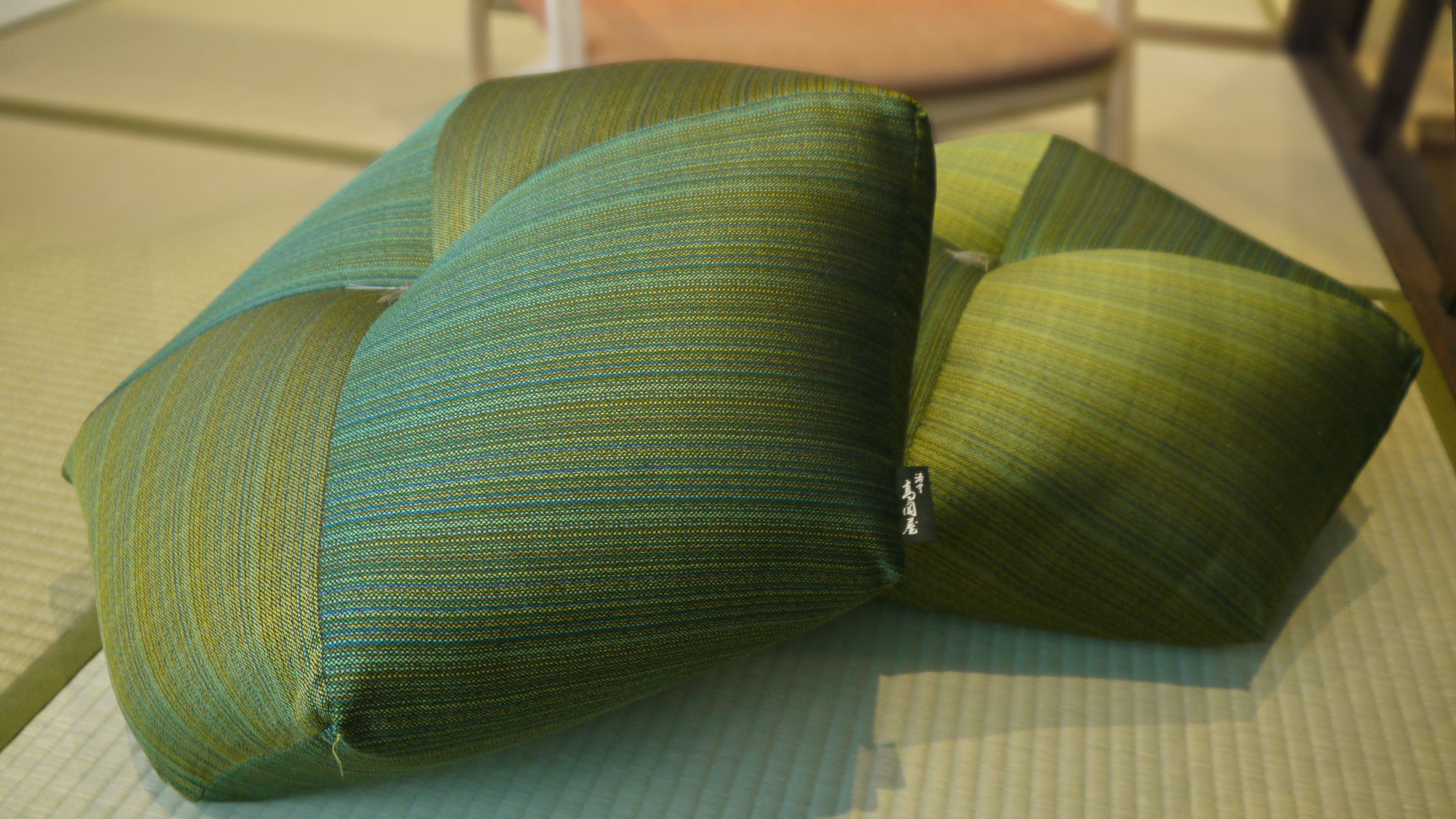 Una butaca verde tapizada con una etiqueta, un cojín y una almohada a juego sobre una superficie con textura.