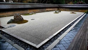 Een traditionele Japanse tuin met een grindpad, rotsen en een houten terras.