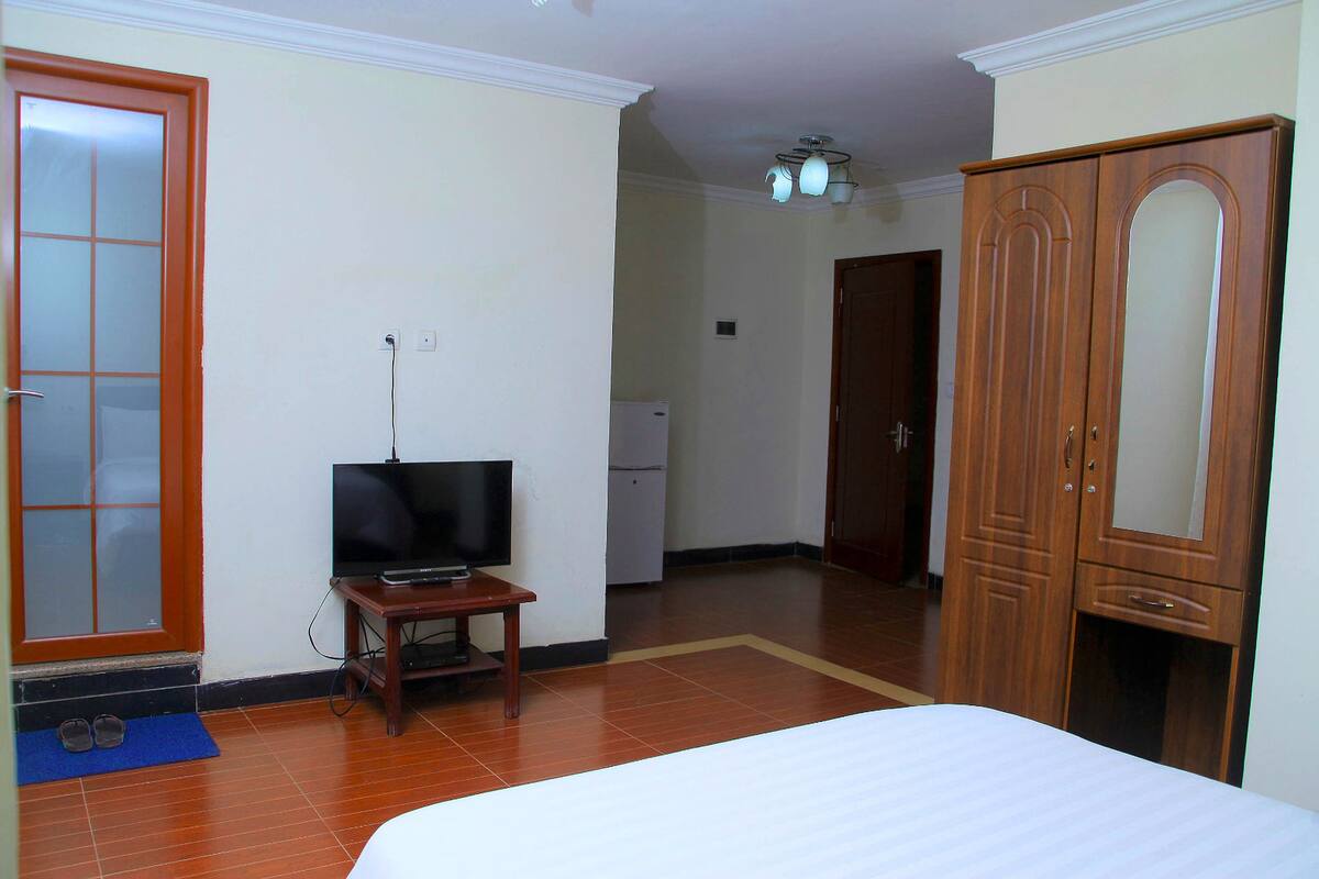 A hotel room with a bed, a television on a small table, a wardrobe, and a door with frosted glass panels.