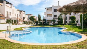 A swimming pool surrounded by a well-maintained lawn and a row of white buildings with balconies. - Lovely apartment in Alcossebre (Alcossebre)