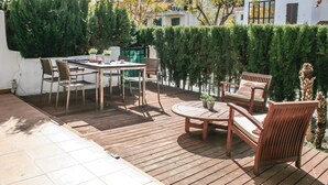 A wooden deck with a table and chairs, surrounded by greenery and a white building in the background. - Lovely apartment in Alcossebre (Alcossebre)