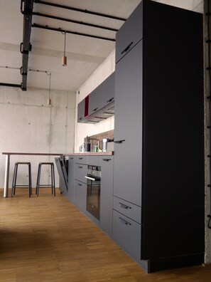 A modern kitchen with grey cabinets, a wooden countertop, and a stainless steel oven. There are two stools and a hanging light fixture.