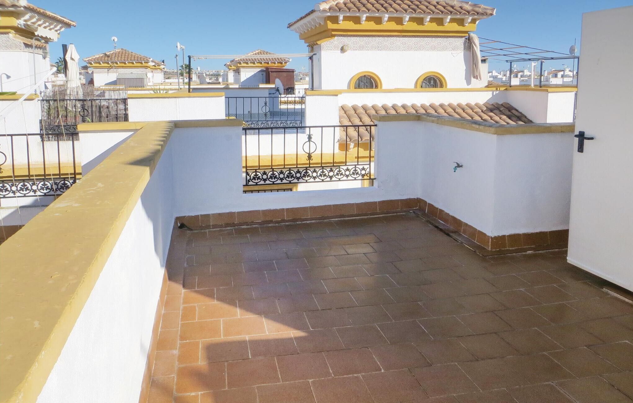 Una terraza en la azotea con suelo de baldosas, una pequeña ventana con rejas de hierro decorativas y una barandilla amarilla.