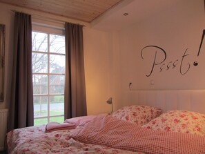 Een slaapkamer met een bed, een raam met gordijnen, een muur met een bord en een radiator.