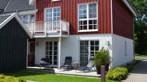 Ein zweistöckiges Haus mit roter Fassade, einem Balkon und einem gepflasterten Auffahrt.