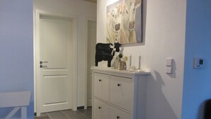 Ein Flur mit einer weißen Tür, einem weißen Schrank mit Schubladen, einem Bild von Kühen und einem Thermostat an der Wand.