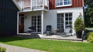 Ein zweistöckiges Haus mit einem Balkon, einer Veranda mit Sitzgelegenheit und einem kleinen Garten.