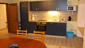 A compact kitchen with dark cabinets, a microwave, an oven, a sink, and a dining table with chairs. - Category C: 3-room apartment for 4 persons - Pension Mühle (Egloffstein)