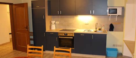 A compact kitchen with dark cabinets, a microwave, an oven, a sink, and a dining table with chairs.