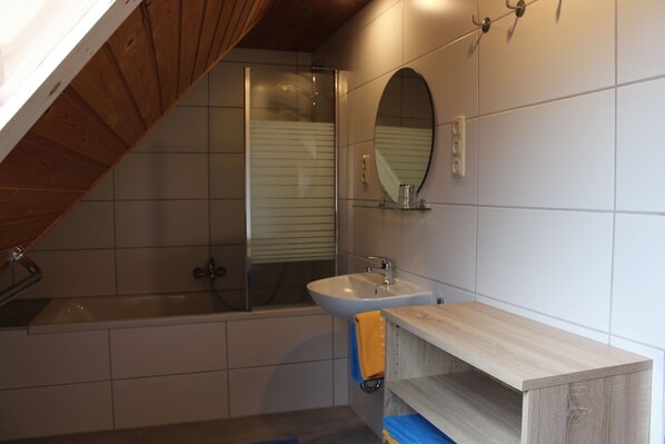 Ein Badezimmer mit Badewanne, Waschbecken, Spiegel und einem Holzregal.